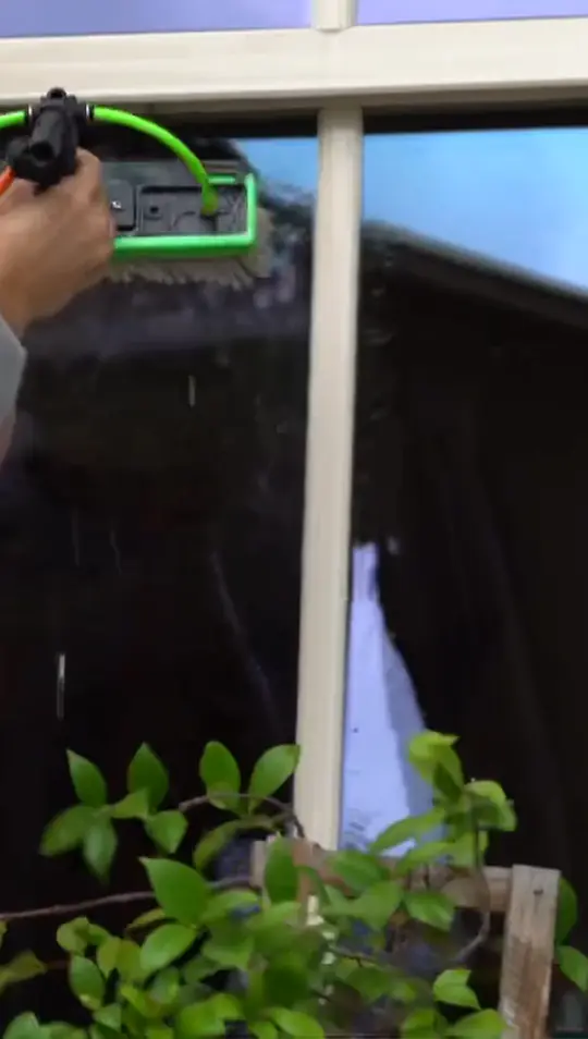 Close view of the pure water brush being worked across a window pane above a planter of greenery