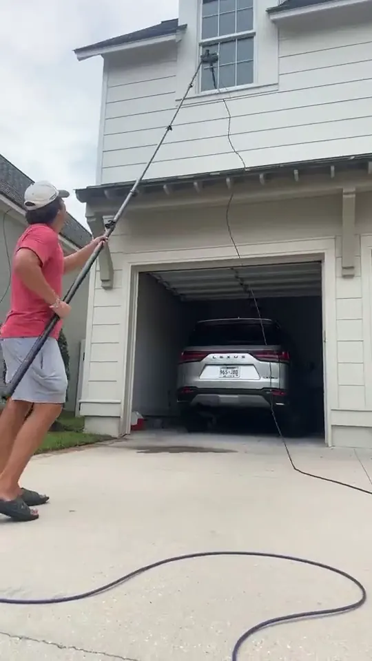 Technician extending a water fed pole to a gable window above a garage door