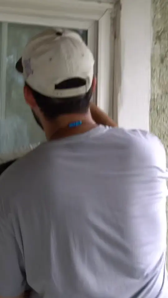 Technician in a branded cap working the upper sash of a window on a cream stucco wall