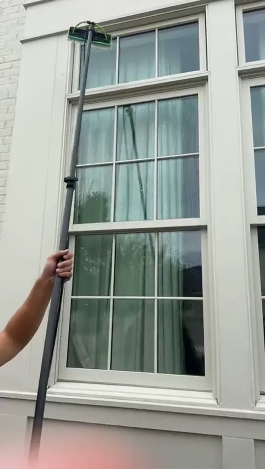 Hands guiding a water fed pole across upper sash windows