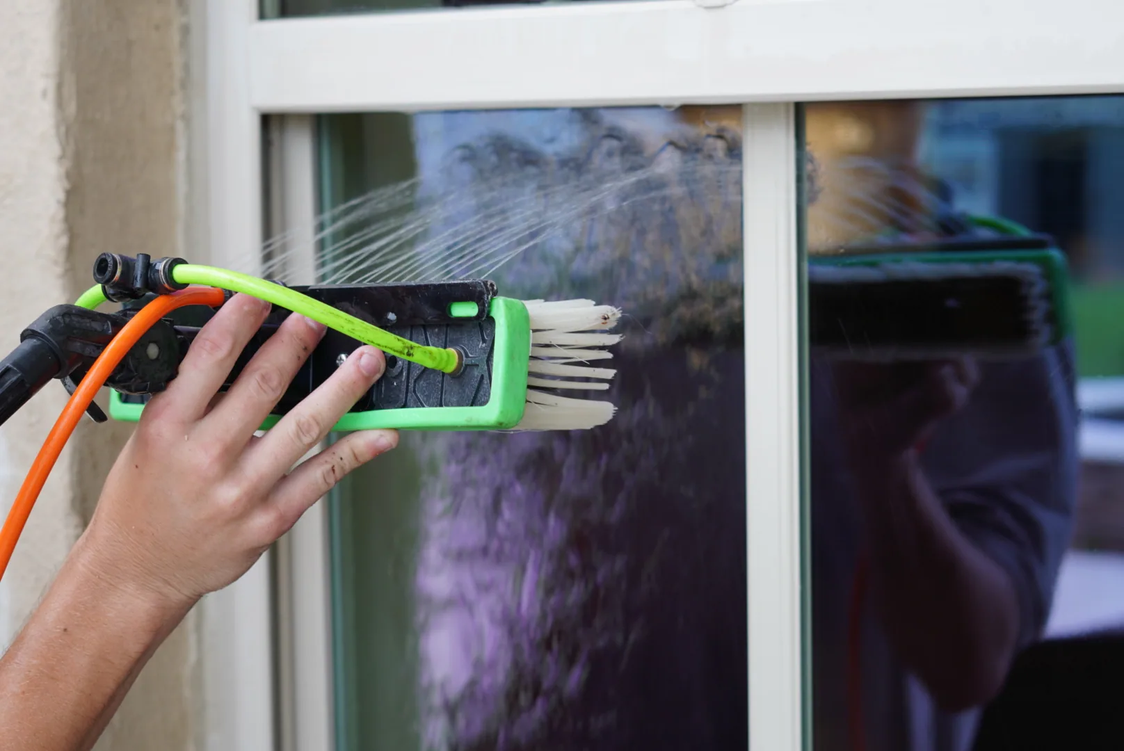 Close up of a hand holding a green pure water brush head spraying water across a window pane.