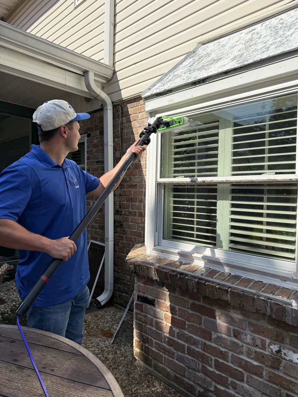 Boot Krewe technician in a blue polo cleaning a window on a brick house