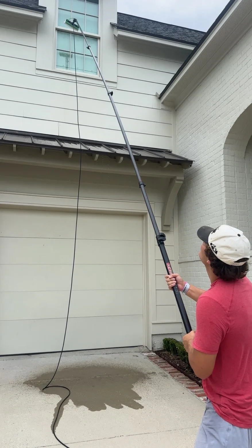 Boot Krewe technician running a water fed pole up to a second storey window over a wet driveway