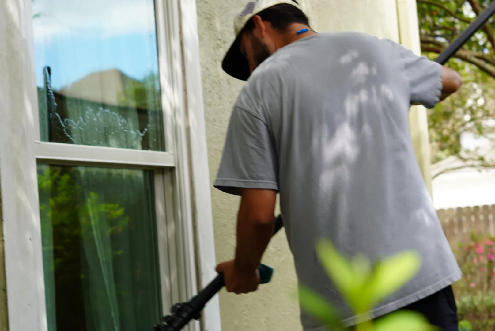 Boot Krewe technician in a branded cap working a pure water brush on a sash window, water running down the pane
